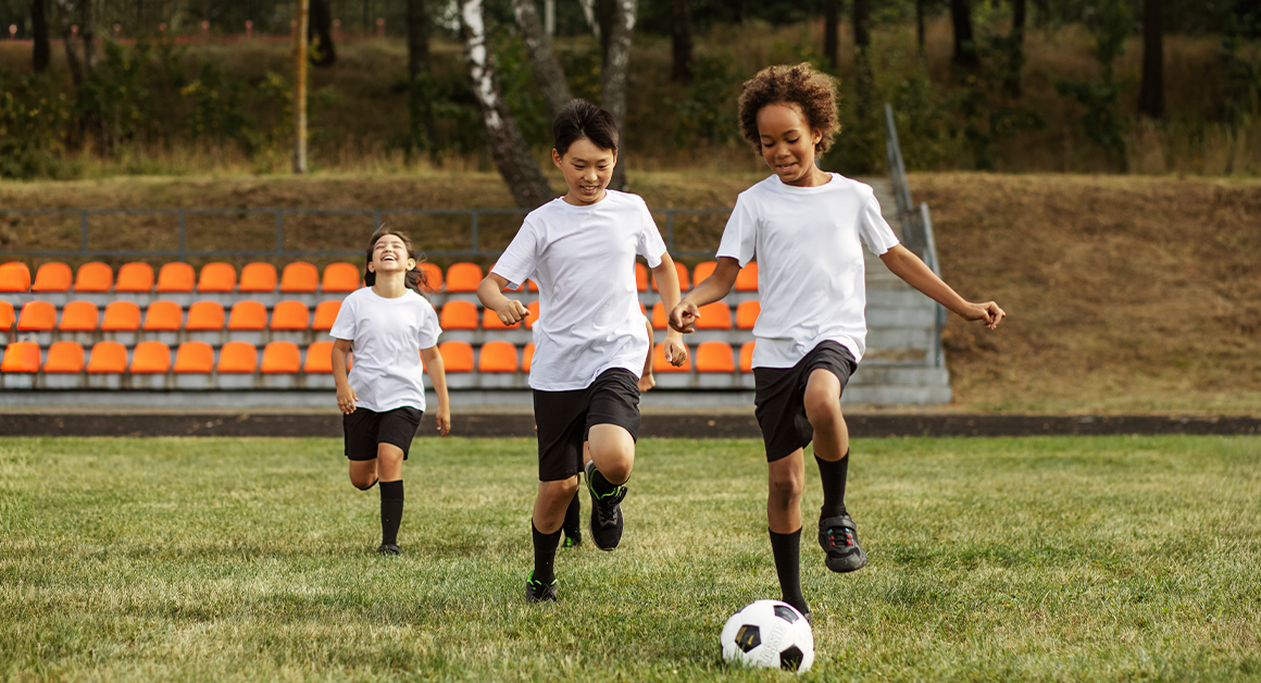 Tres niños jugando fútbol en un campo lleno de paso, representando buena salud física.