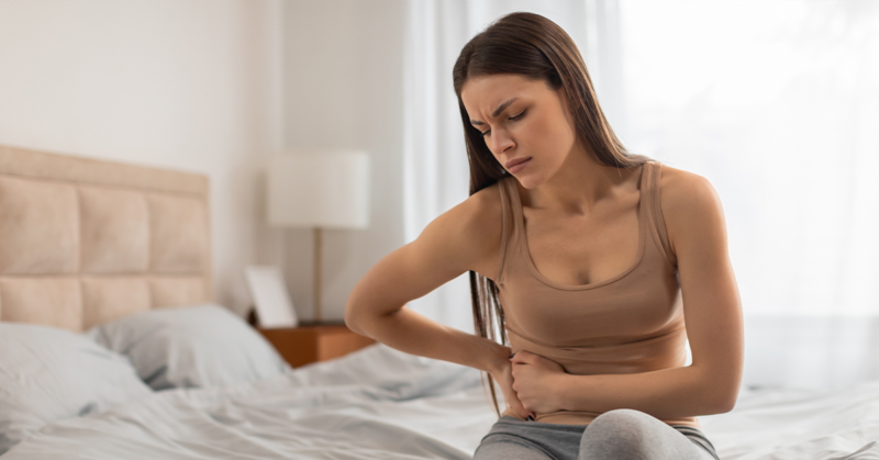 Mujer sosteniendo la parte baja del abdomen por dolor, representando causas comunes de malestar abdominal o cólicos.