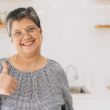 Señora mayor sonríe y muestra un pulgar arriba en medio de una cocina iluminada.