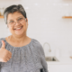 Señora mayor sonríe y muestra un pulgar arriba en medio de una cocina iluminada.