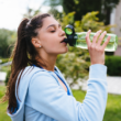 Una mujer con ropa deportiva toma agua al aire libre, representando una correcta hidratación en temporada de calor.
