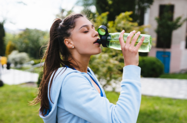 Una mujer con ropa deportiva toma agua al aire libre, representando una correcta hidratación en temporada de calor.