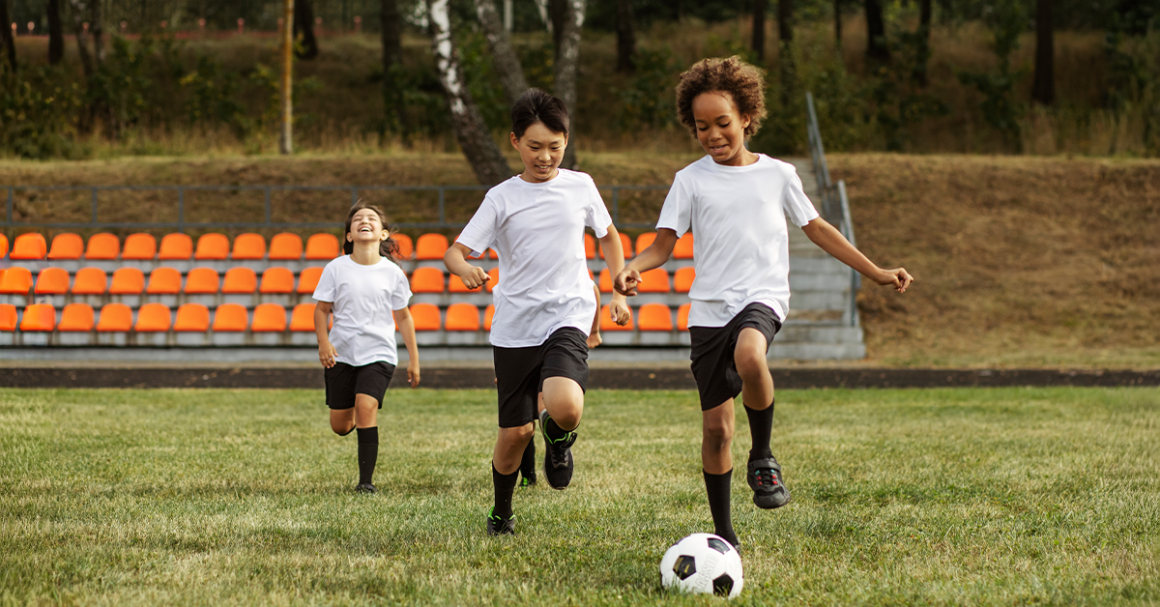 Tres niños jugando fútbol en un campo lleno de paso, representando buena salud física.