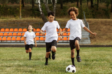 Tres niños jugando fútbol en un campo lleno de paso, representando buena salud física.