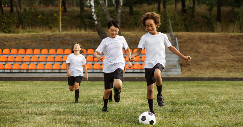 Tres niños jugando fútbol en un campo lleno de paso, representando buena salud física.