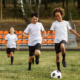 Tres niños jugando fútbol en un campo lleno de paso, representando buena salud física.