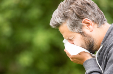 Hombre al aire libre sonándose la nariz con un pañuelo blanco.