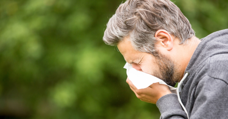 Hombre al aire libre sonándose la nariz con un pañuelo blanco.