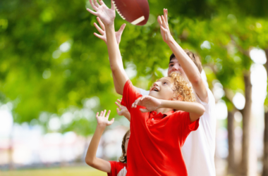Escena energética de niños jugando a atrapar un balón de fútbol, rodeados de árboles en un parque.