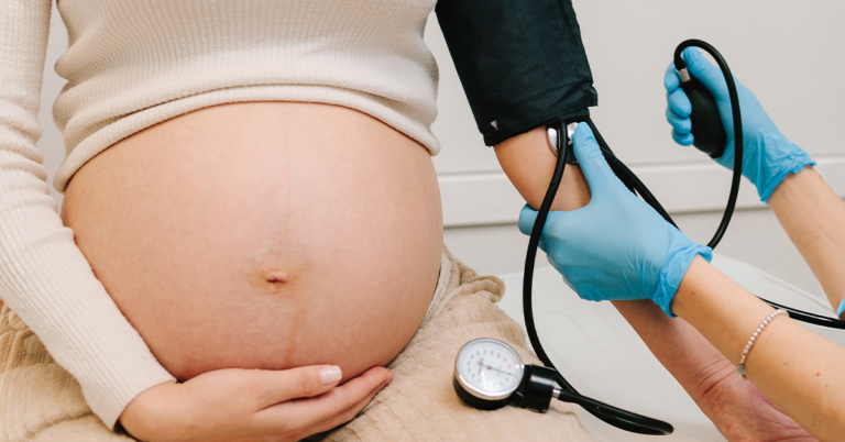 Healthcare provider measures a pregnant person's blood pressure during a prenatal checkup.