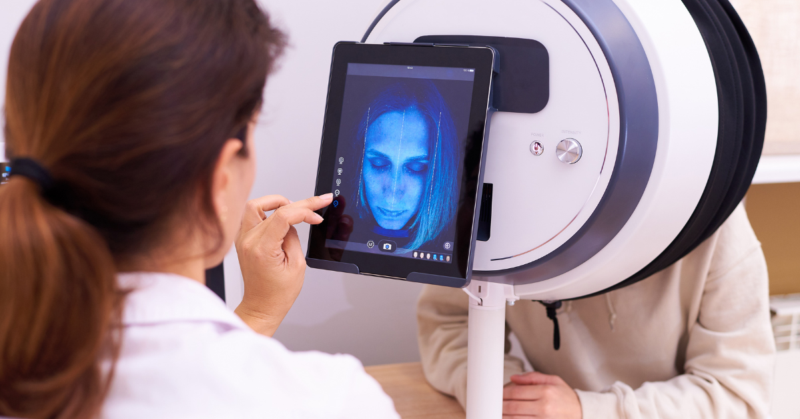 Una dermatóloga revisando la piel de una persona a través de una máquina de análisis facial.