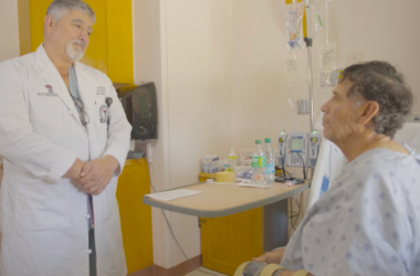 El Dr. Philip E. Fiddler, Director del UMC Burn Center, habla con Javier Diaz, un paciente sentado en la cama de un hospital. La habitación está llena de equipo médico.