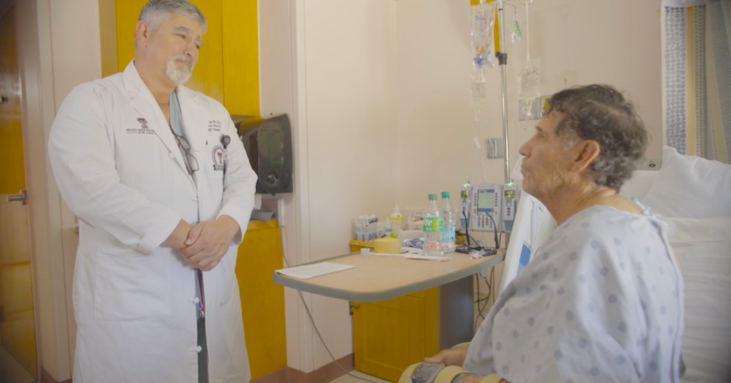 El Dr. Philip E. Fiddler, Director del UMC Burn Center, habla con Javier Diaz, un paciente sentado en la cama de un hospital. La habitación está llena de equipo médico.