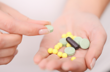 Una mano sostiene varias pastillas: tabletas verdes, píldoras amarillas y una cápsula negra. Otra mano sostiene una tableta verde, representando el uso seguro de antibióticos.