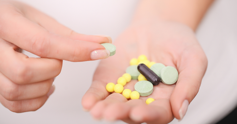 Una mano sostiene varias pastillas: tabletas verdes, píldoras amarillas y una cápsula negra. Otra mano sostiene una tableta verde, representando el uso seguro de antibióticos.