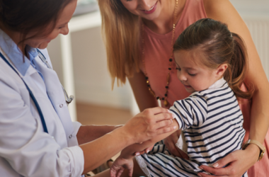 Un profesional de la salud se prepara para vacunar a una niña pequeña, mientras su madre la sostiene.