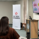Hombre presenta ante un grupo de asistentes junto a un banner de El Paso Chamber y una pantalla con un diagrama por pasos